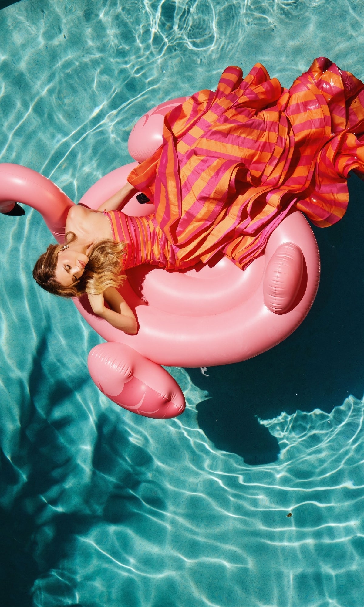 Someone wearing the Ava Presley 40119 long formal dress relaxes on a pink flamingo-shaped inflatable pool float in a swimming pool.